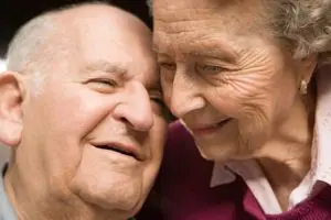 An older couple is smiling and touching each other.